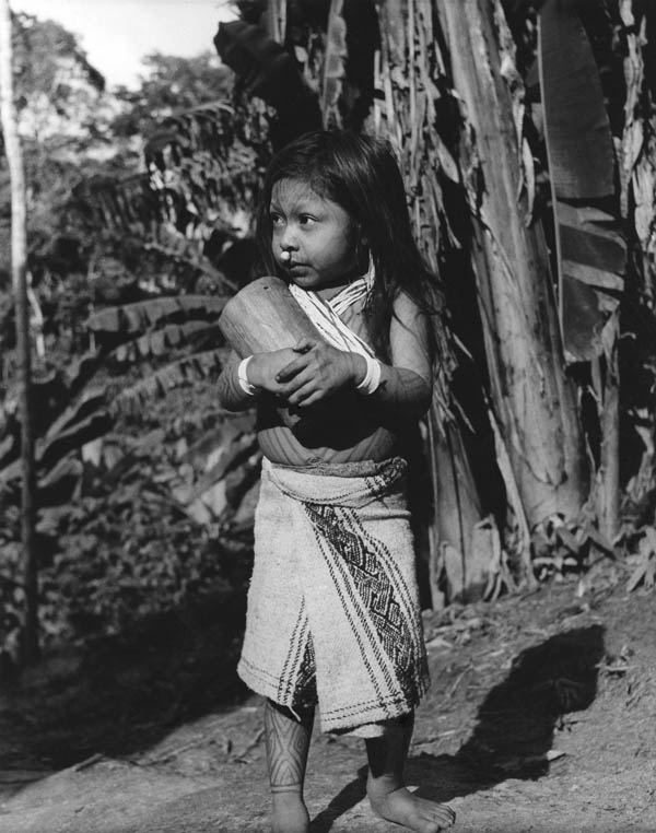 Baxi, a Cashinahua girl with her wooden doll (note the carved eyes and mouth).  The designs painted on her body fade after about a week. Peru, 1957. Photograph by Kenneth M. Kensinger. Penn Museum image #148803
